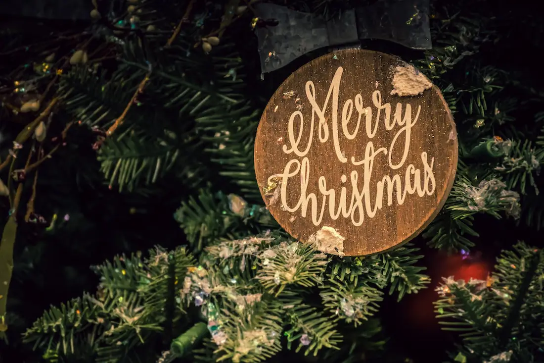 Placa redonda con mensaje Merry Christmas sobre árbol de Navidad